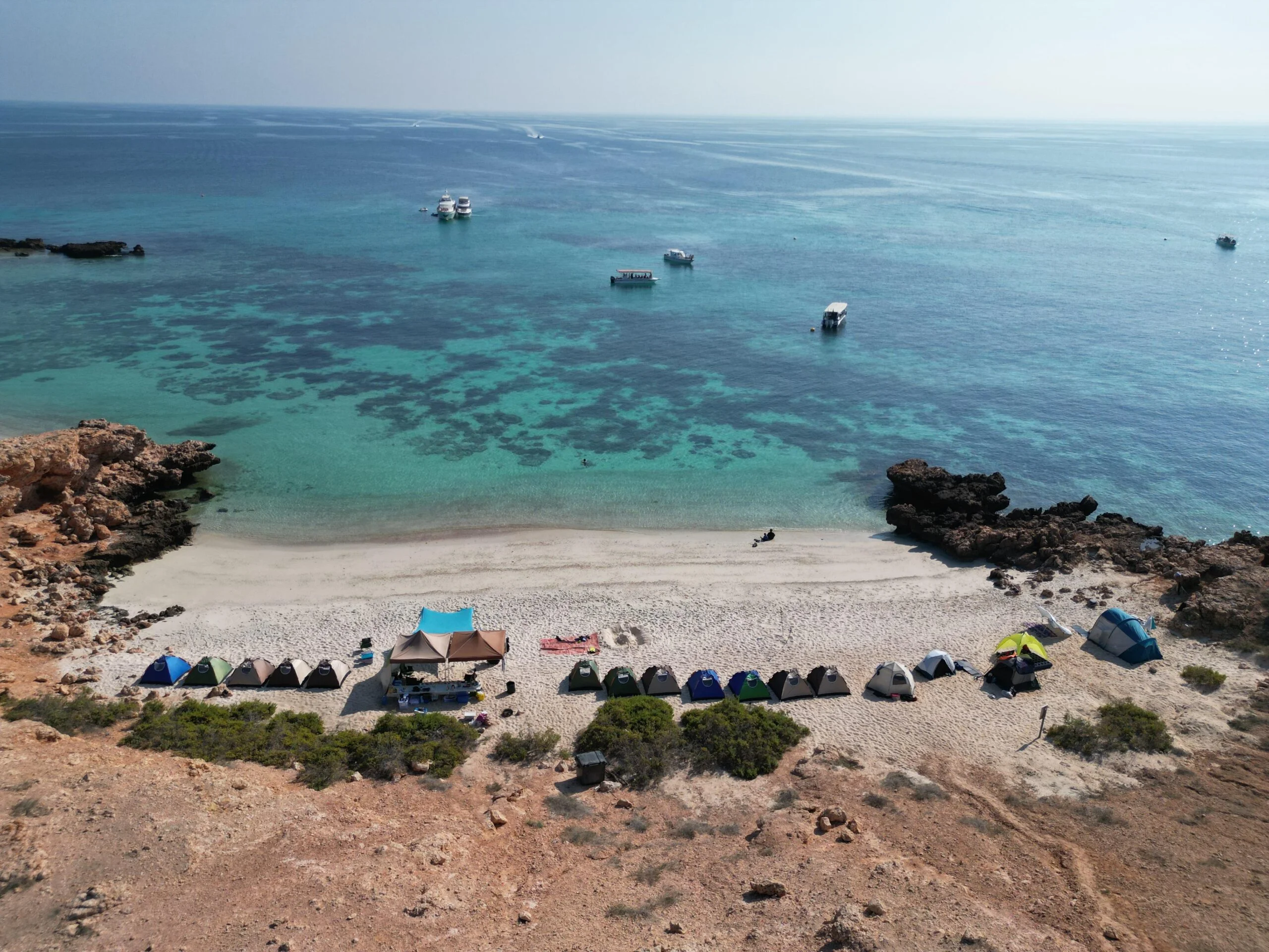 Tents on the beach of a Daymaniyat island with boats offshore